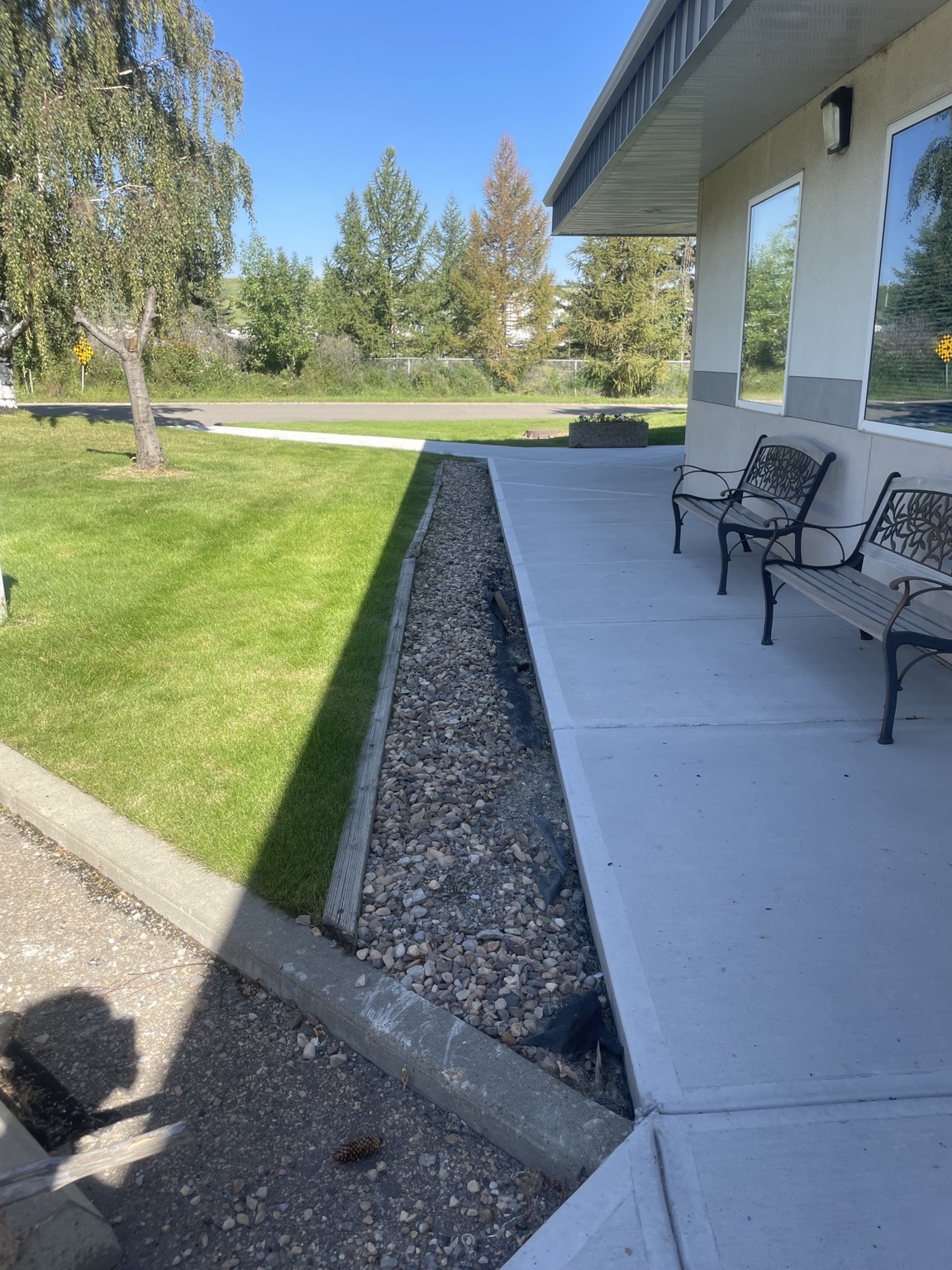 Narrow rock bed beside a concrete walkway with exposed landscape fabric and uneven rock coverage before Cedarline's refresh